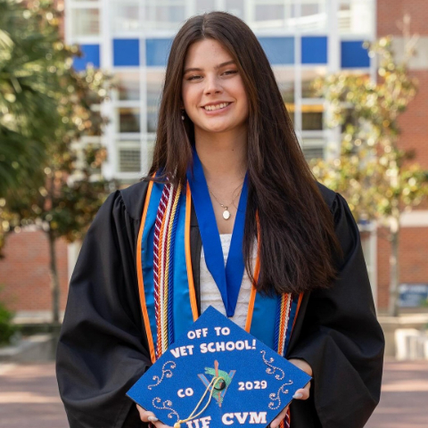 Woman in a graduation robe with a blue sash in front of the Ben Hill Griffin Stadium